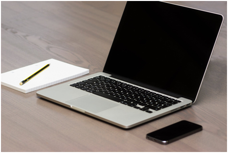 Mac, notepad, pen, and phone on a table