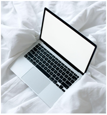 Apple laptop on bed with white sheets