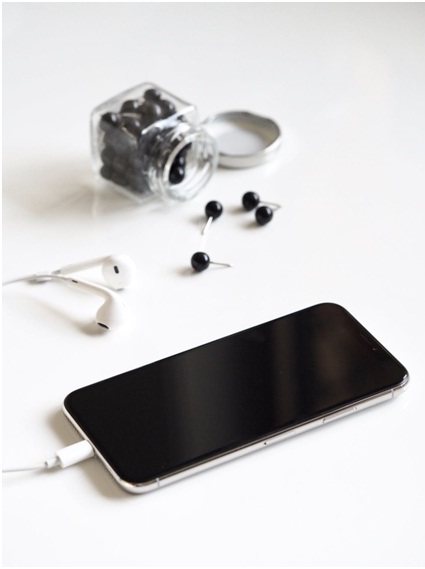 Black pins in jar spilled next to iPhone with headphones plugged into it