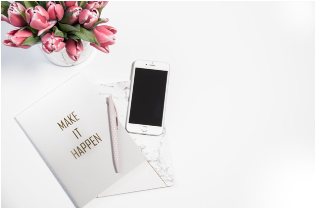 pink flowers, an iPhone, and a notebook with a pen